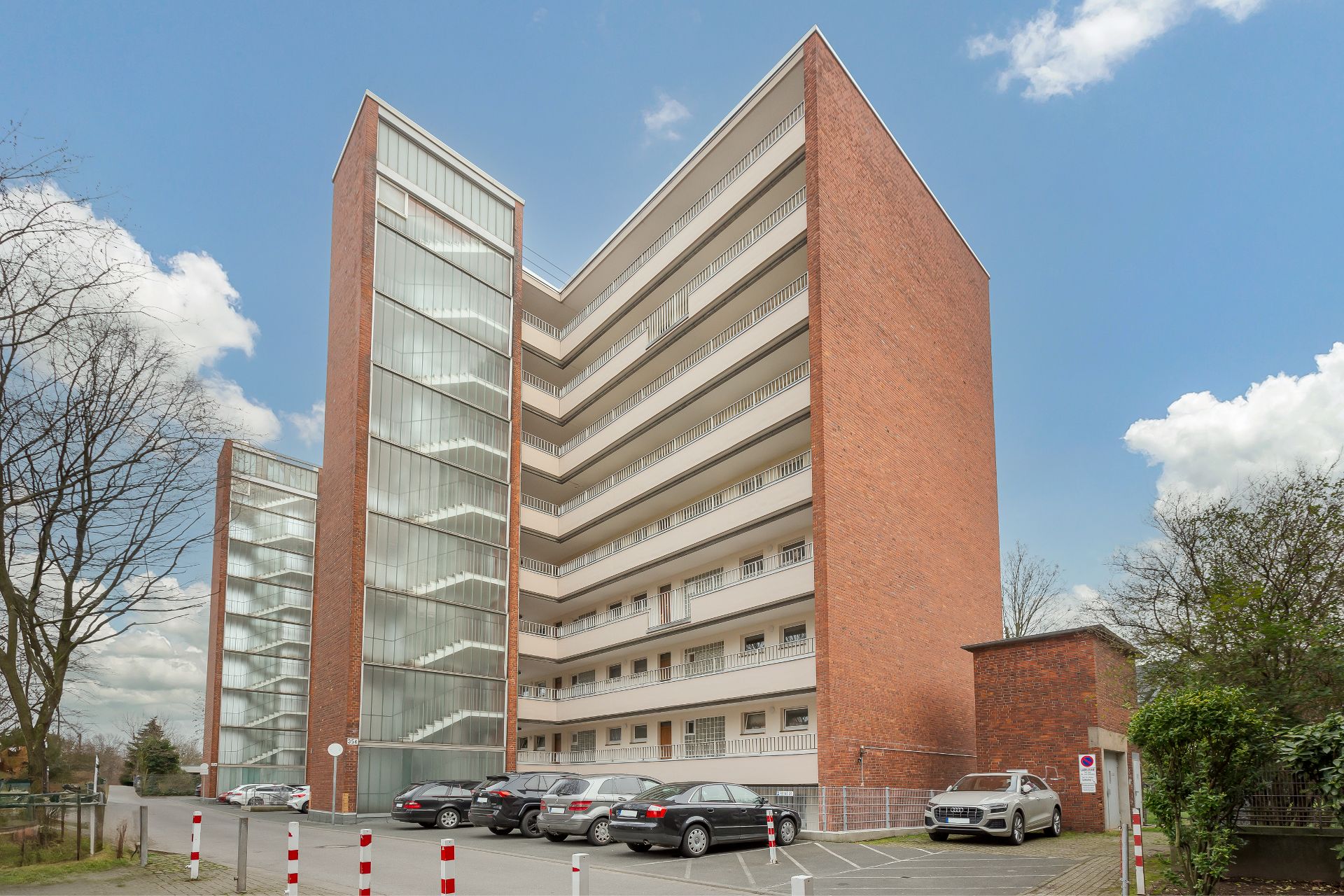 Mehrstöckiges Wohngebäude mit Balkonen und Parkplätzen im Vordergrund.