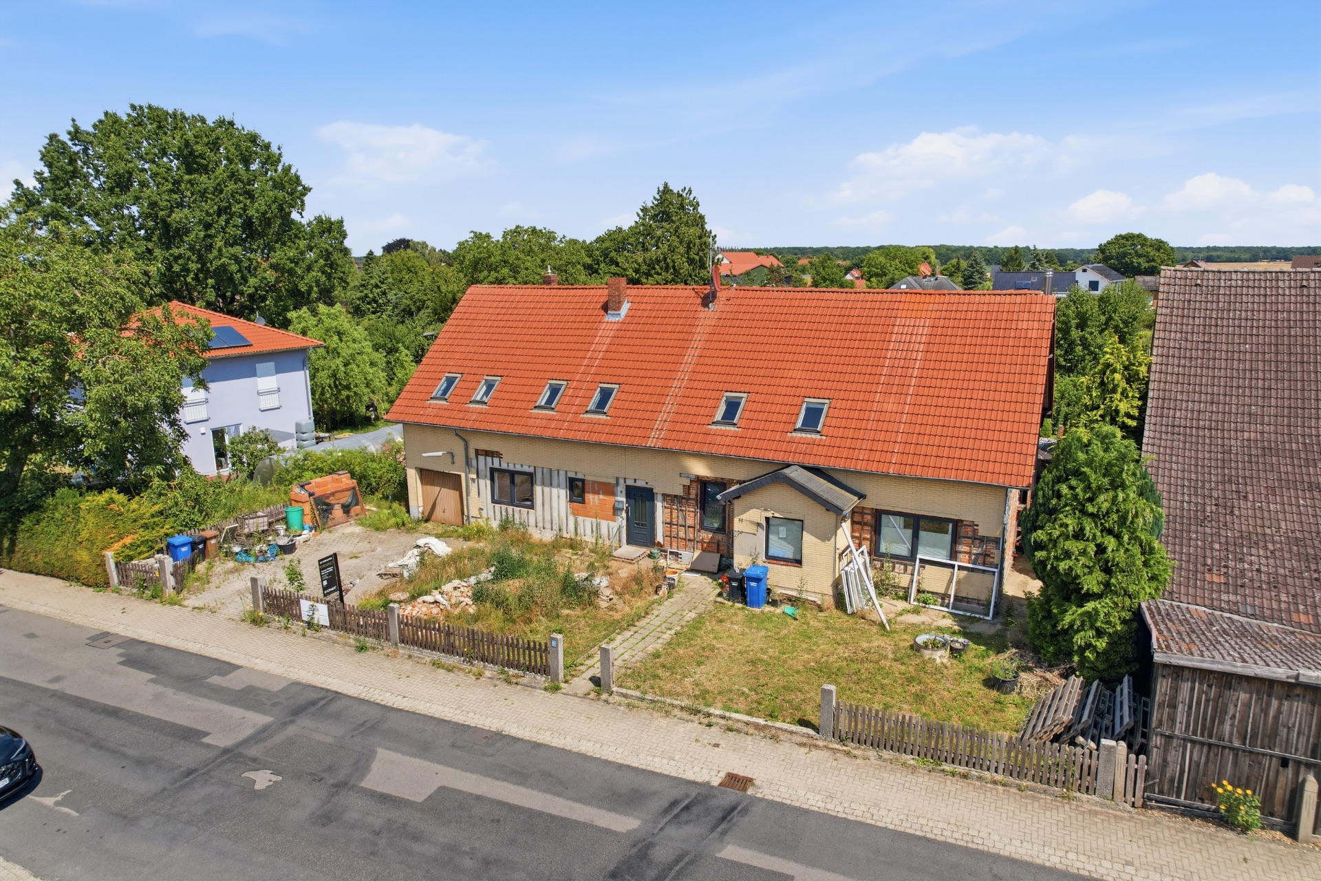 Doppelhaushälfte mit rotem Dach, Vorgarten und Zaun an einer ruhigen Straße.