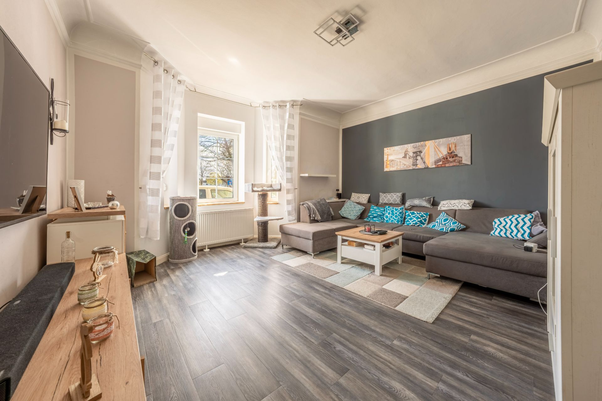 Modernes Wohnzimmer mit großer Eckcouch, Couchtisch, Wandbild und Fenster mit weißen Vorhängen.