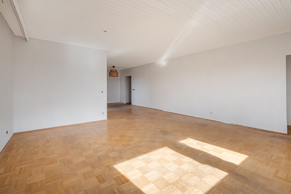 Leerer heller Raum mit Parkettboden, weißen Wänden und Deckenlampe.