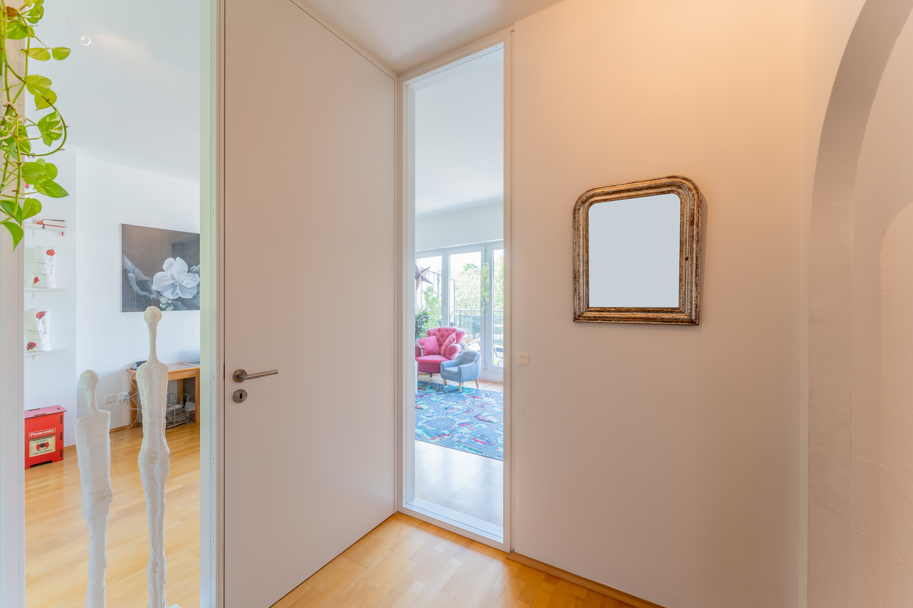 Heller Flur mit großem Spiegel, Holzboden und Blick in ein buntes Wohnzimmer.