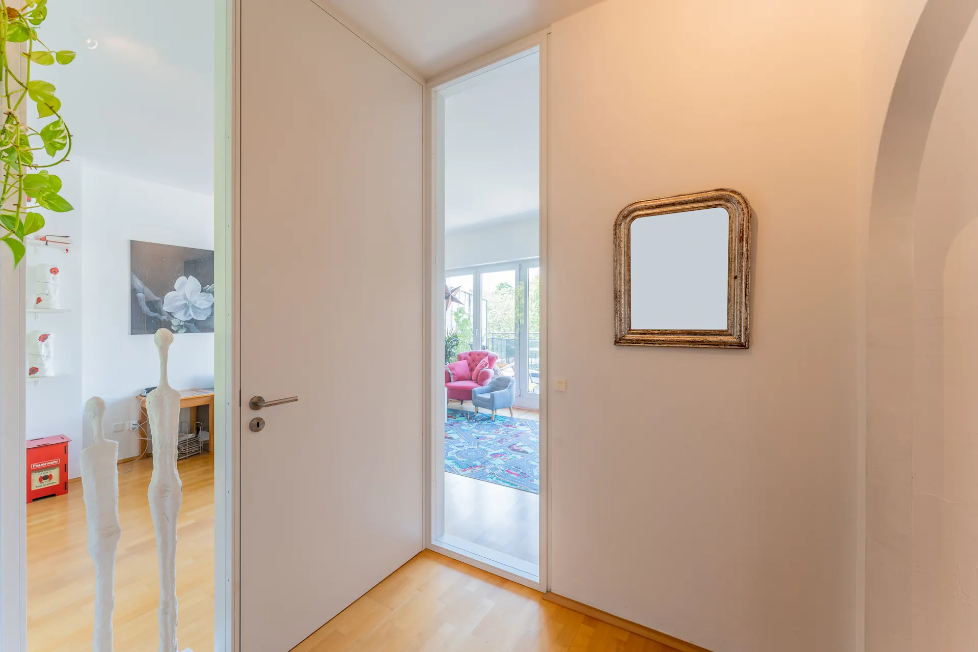 Heller Flur mit großem Spiegel, Holzboden und Blick in ein buntes Wohnzimmer.