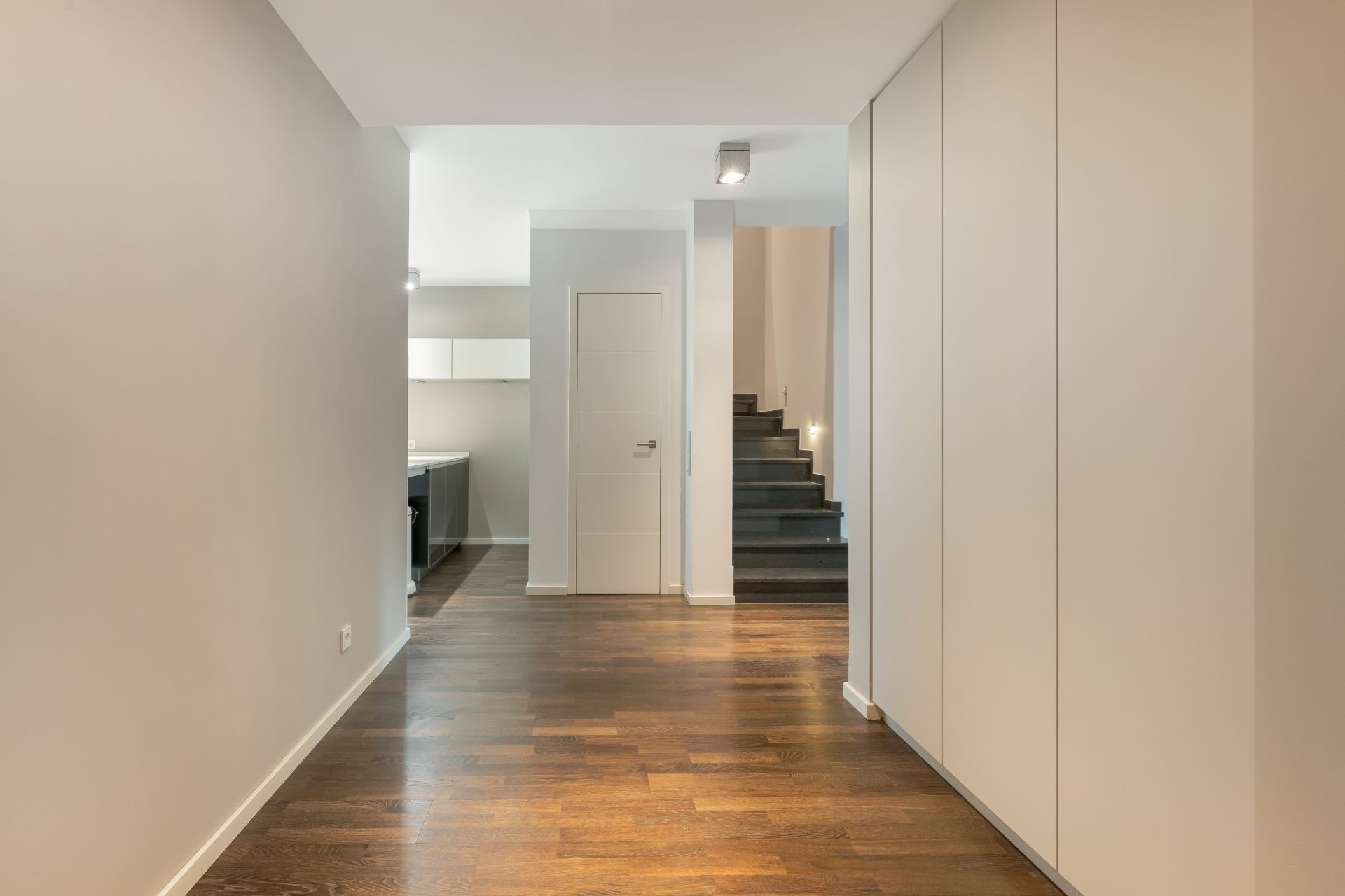 Heller Flur mit Holzboden, weißen Wänden, Einbauschränken und Treppe im Hintergrund.