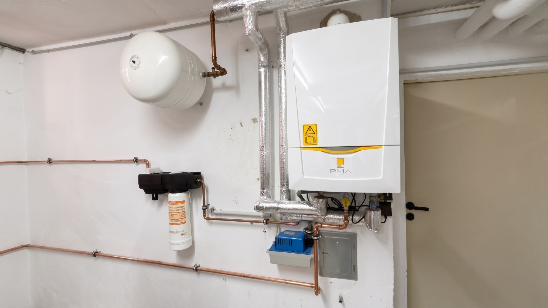 Moderne Heizungsanlage mit Rohren und Druckbehälter an einer weißen Wand.