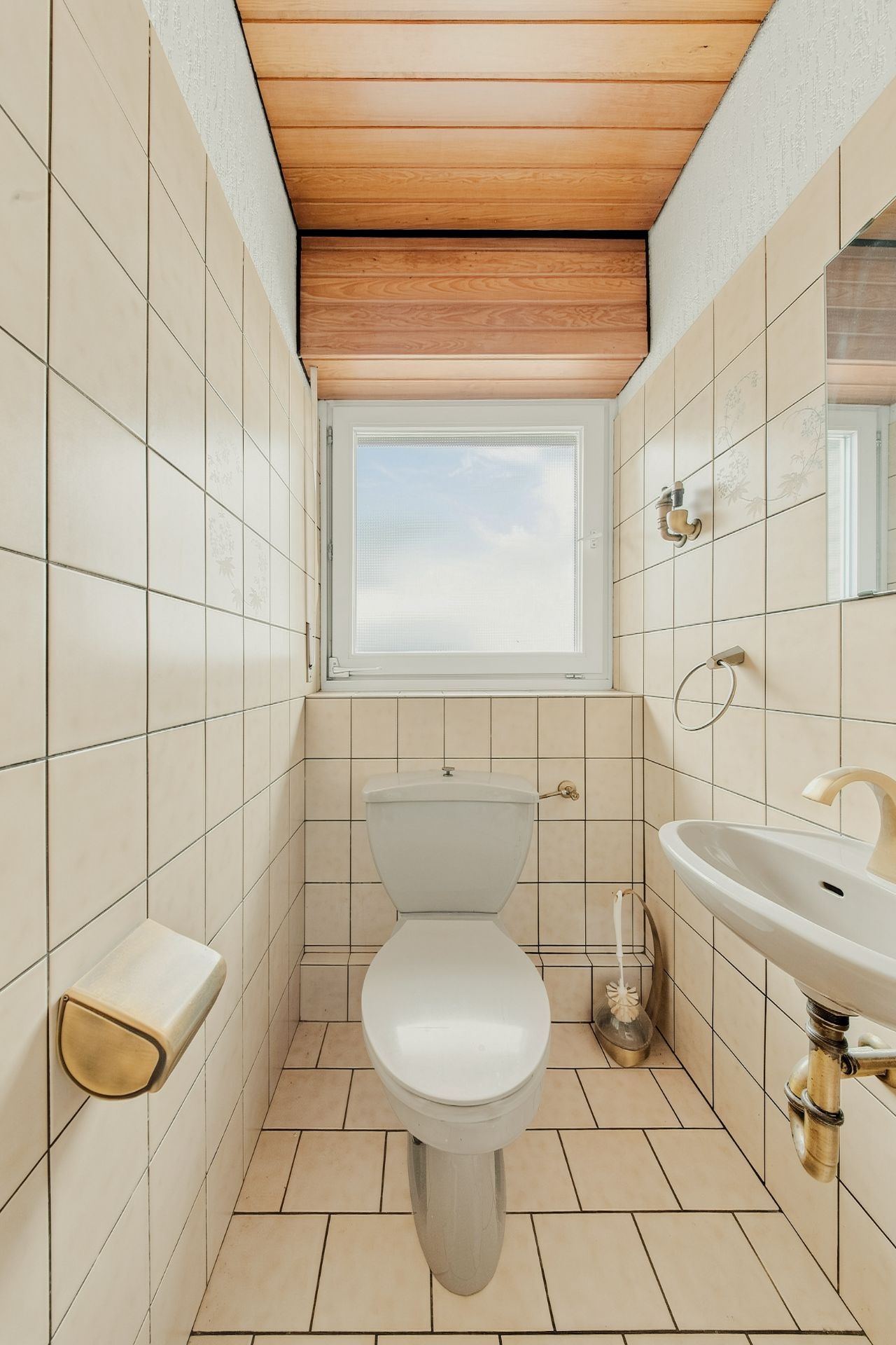 Kleines, gefliestes Badezimmer mit Toilette, Waschbecken und Fenster.