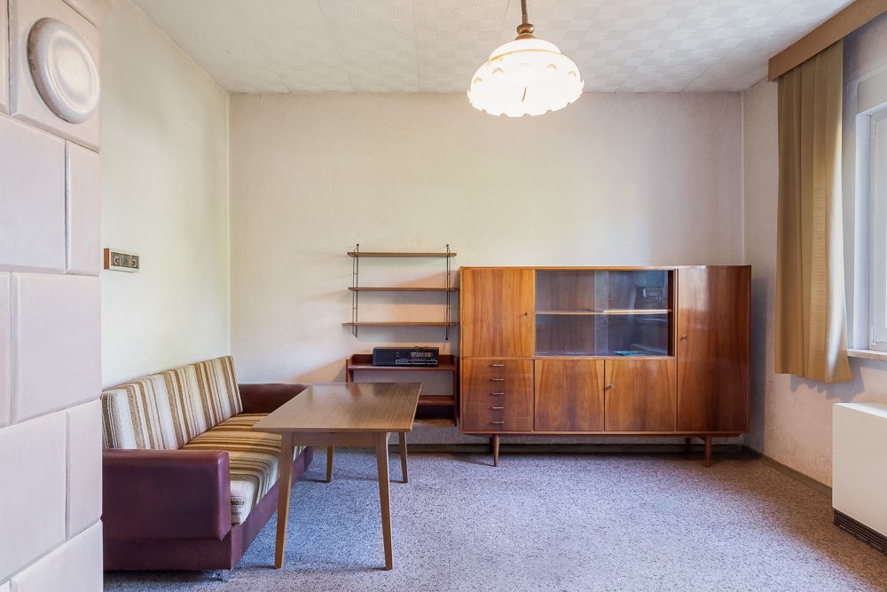 Wohnzimmer mit Sofa, Holztisch, Sideboard, Regal und großem Fenster mit Vorhang.