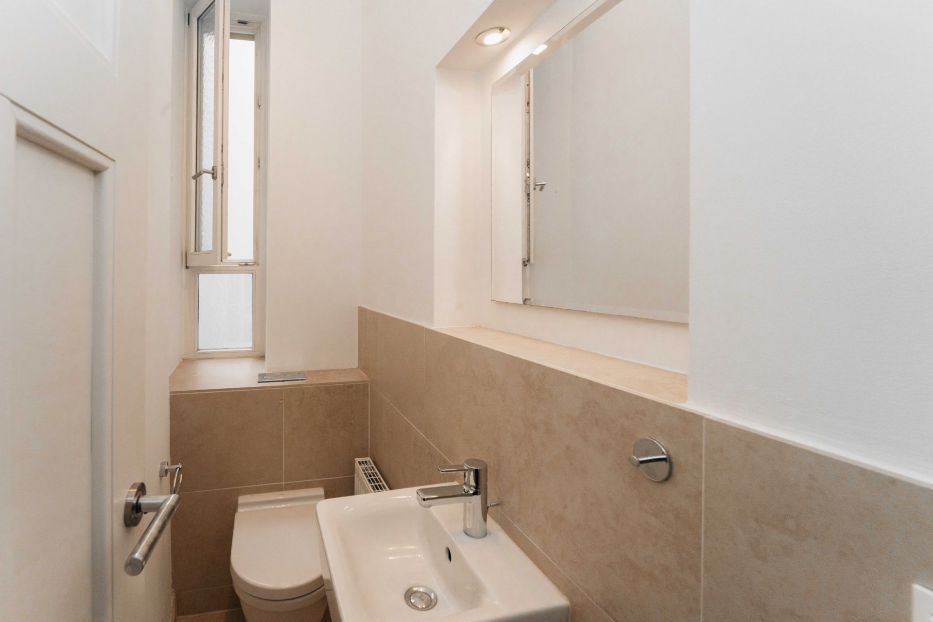 Kleines Badezimmer mit WC, Waschbecken, Fenster und Spiegel.