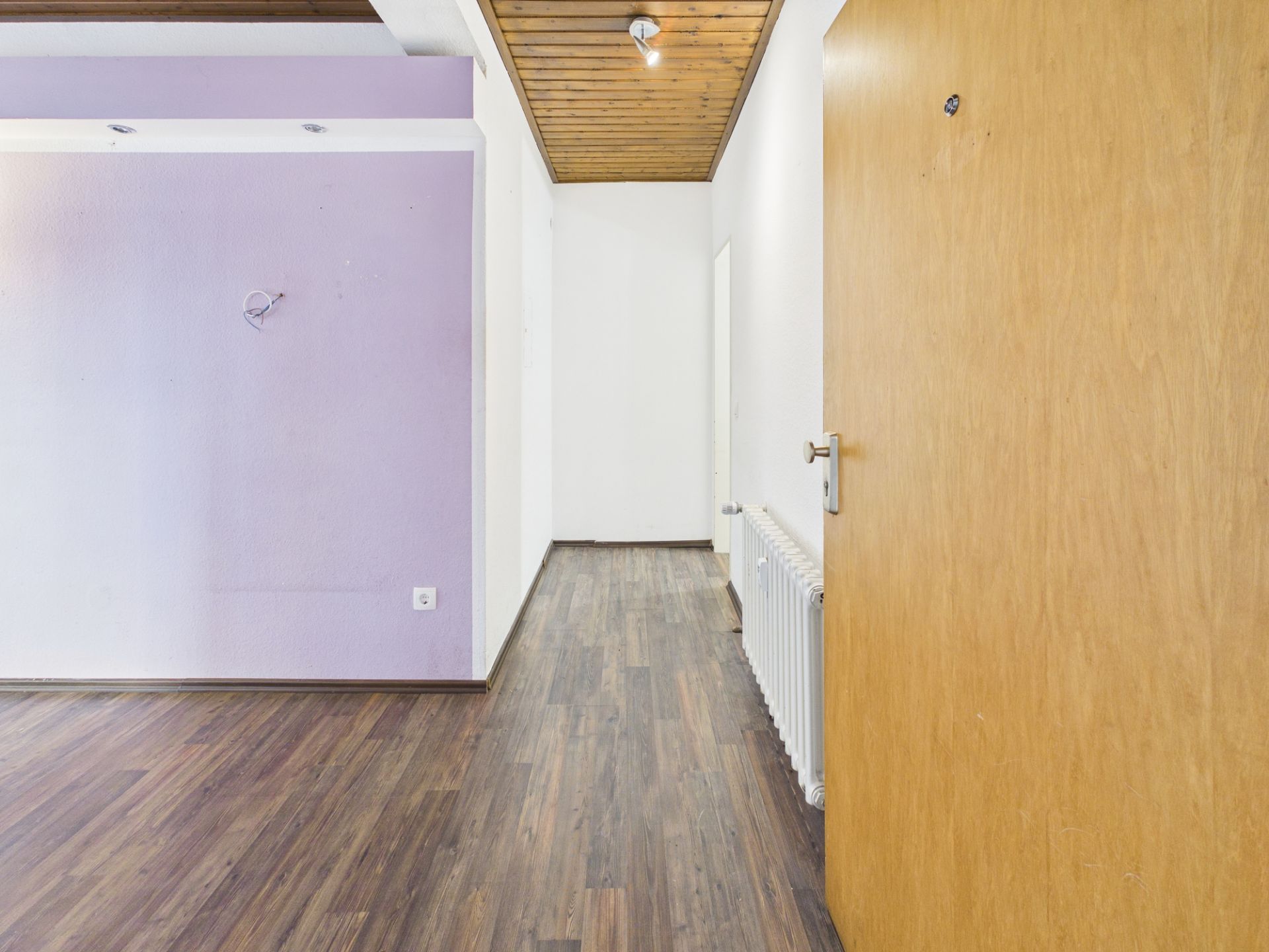 Flur mit Holzboden, heller Wand, lila Akzentwand und offen stehender Holztür.