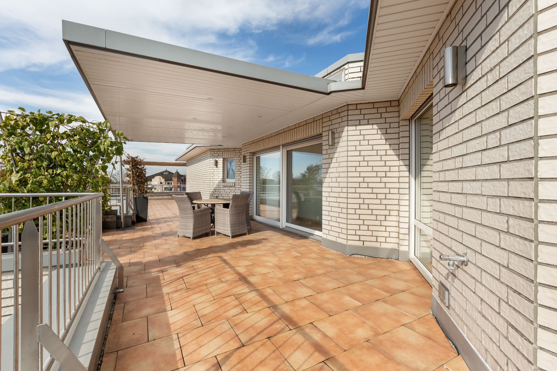 Große Terrasse mit Fliesenboden, Sitzgruppe, Pflanzkübeln und Glas-Schiebetüren an einem Wohnhaus.