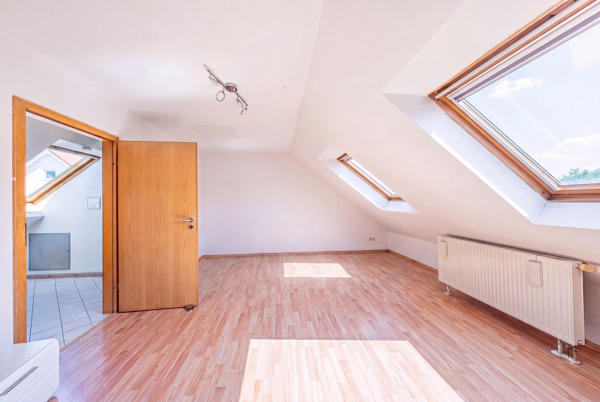 Heller Dachraum mit Holzfußboden, großen Dachfenstern und offen stehender Tür.