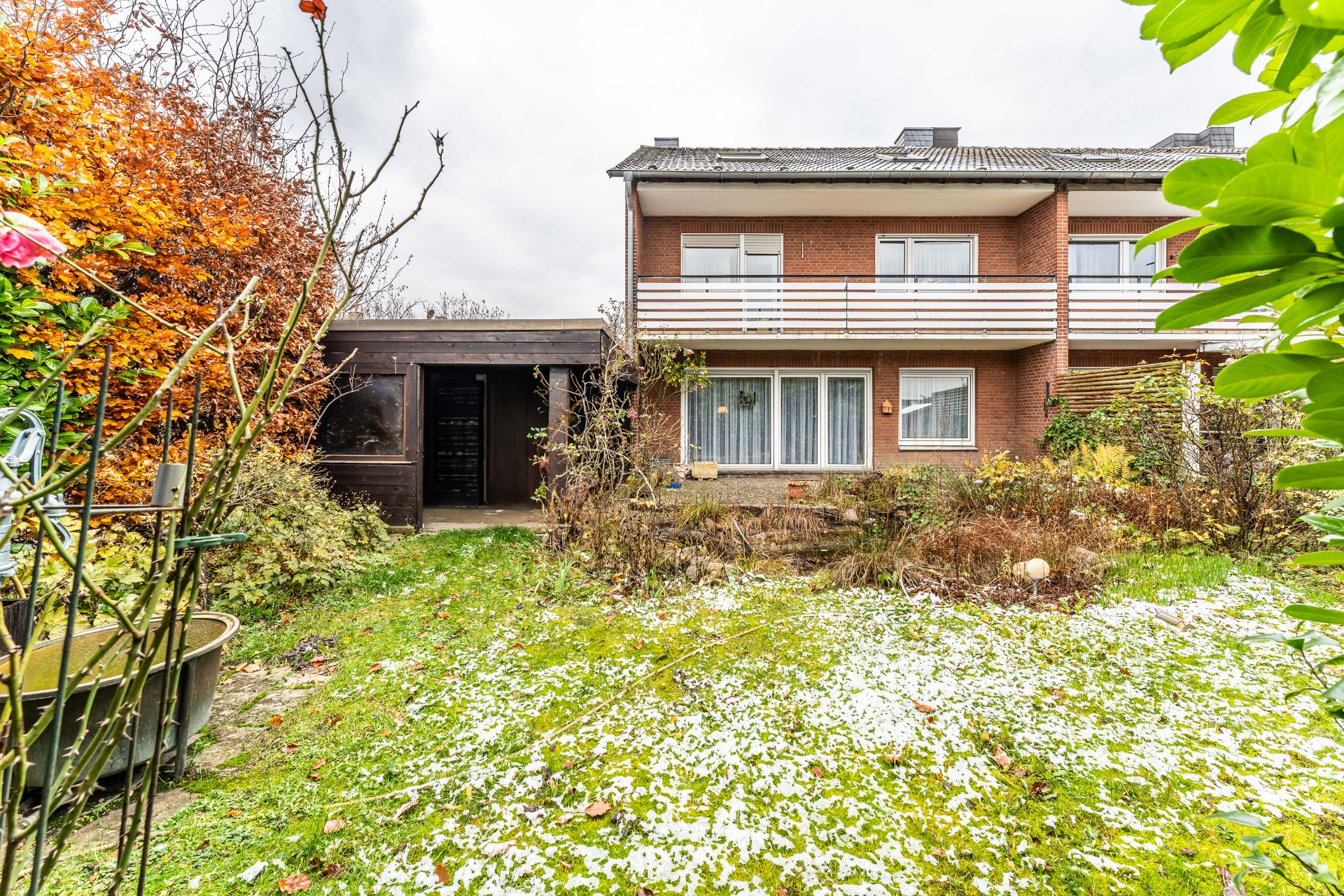 Garten mit etwas Schnee, Sträuchern und Blick auf ein zweistöckiges Wohnhaus mit Balkon.