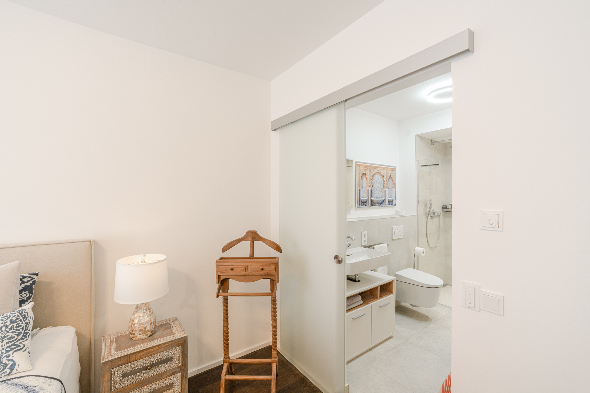Blick vom Schlafzimmer ins Badezimmer mit Schiebetür, Nachttisch und Kleiderständer.