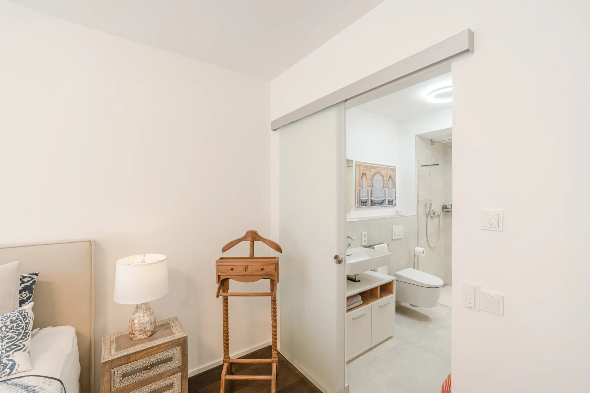 Blick vom Schlafzimmer ins Badezimmer mit Schiebetür, Nachttisch und Kleiderständer.