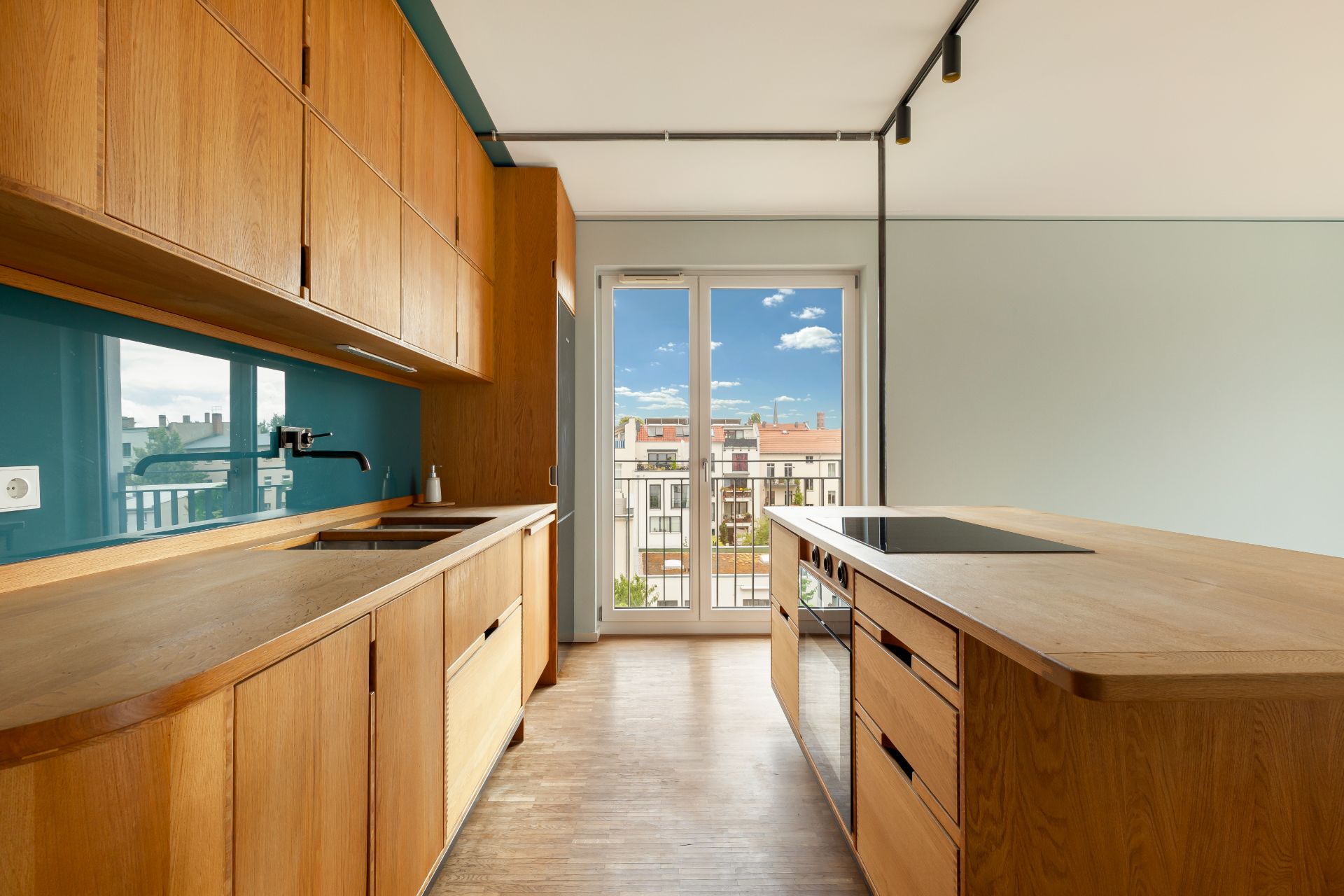 Moderne Küche mit Holzmöbeln, Kochinsel und großem Fenster mit Blick auf einen Balkon.