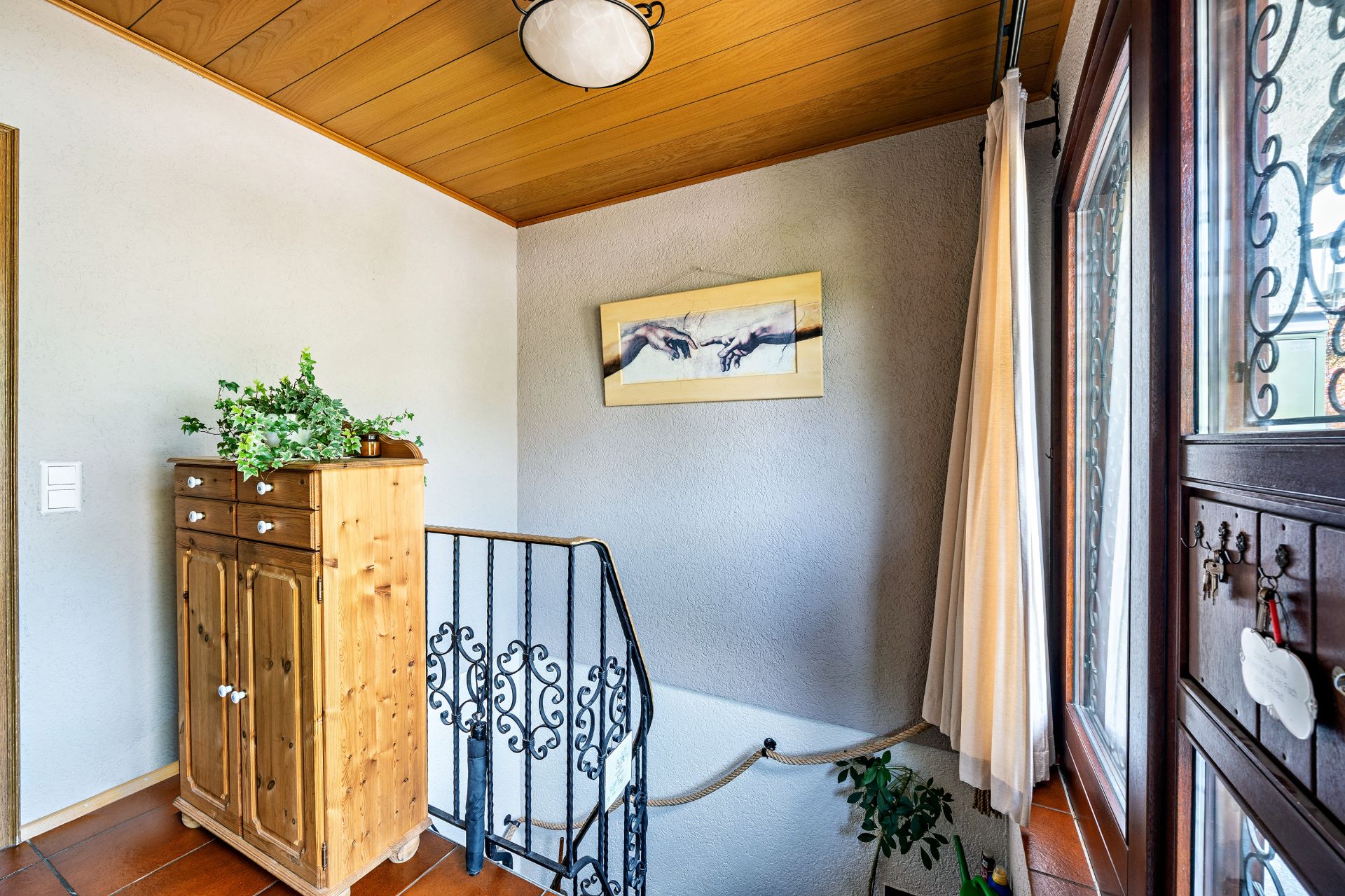 Heller Flur mit Holzdecke, Kommode, Pflanze, Metallgeländer und Bild an der Wand.