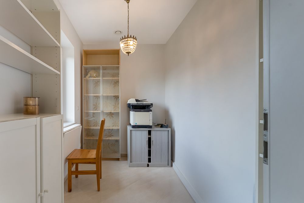 Kleiner Raum mit Regal, Holzstuhl, Schrank, Drucker und Hängelampe.