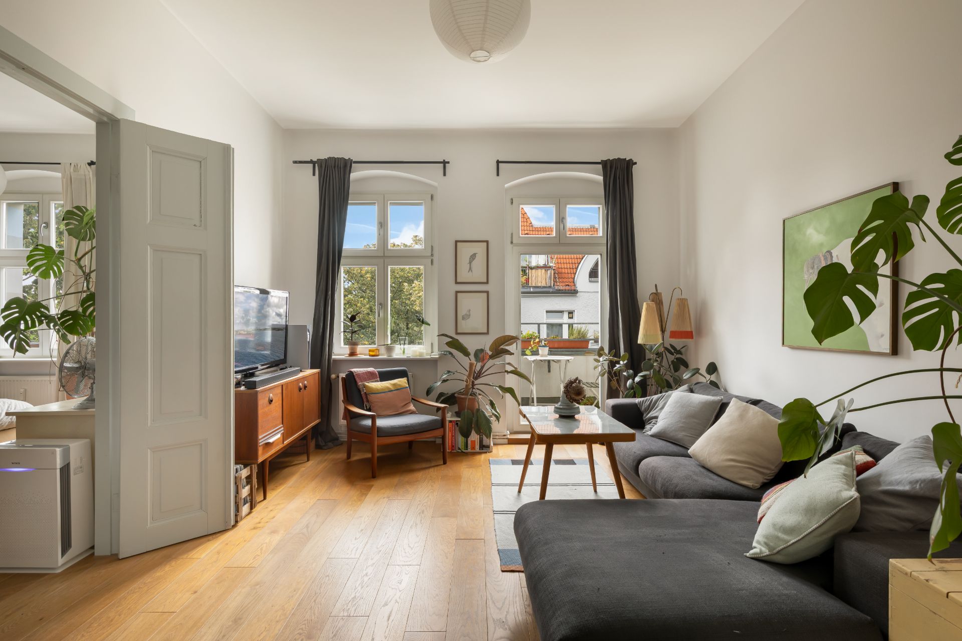 Helles Wohnzimmer mit Holzfußboden, Sofa, Sessel, Couchtisch und Zimmerpflanzen.