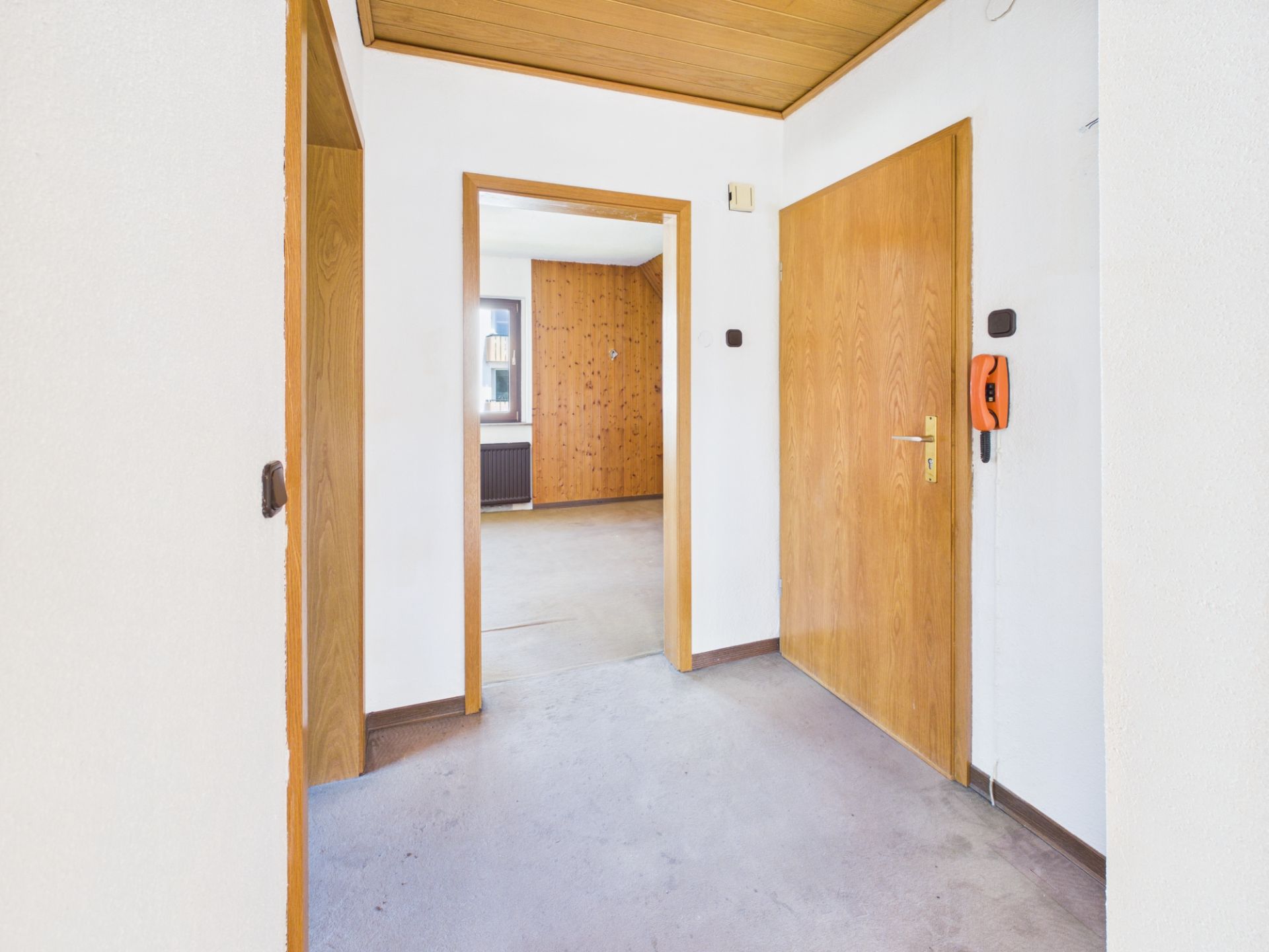 Heller Flur mit Holztüren und Sicht auf ein weiteres Zimmer mit Holzverkleidung.