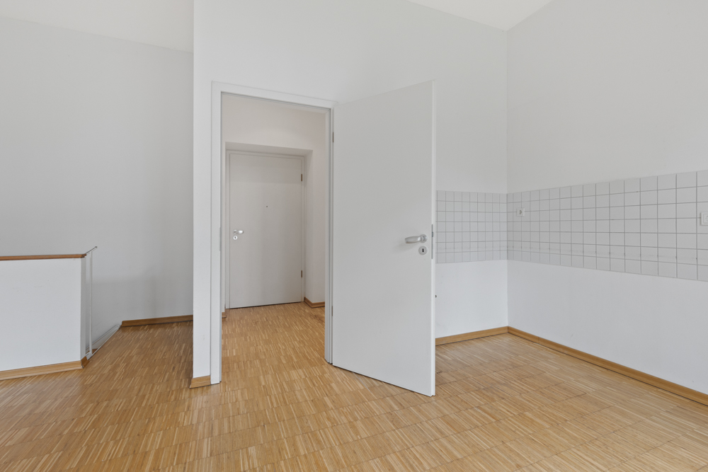 Leerer Raum mit Holzboden, weißer Tür und weiß gefliester Wand.