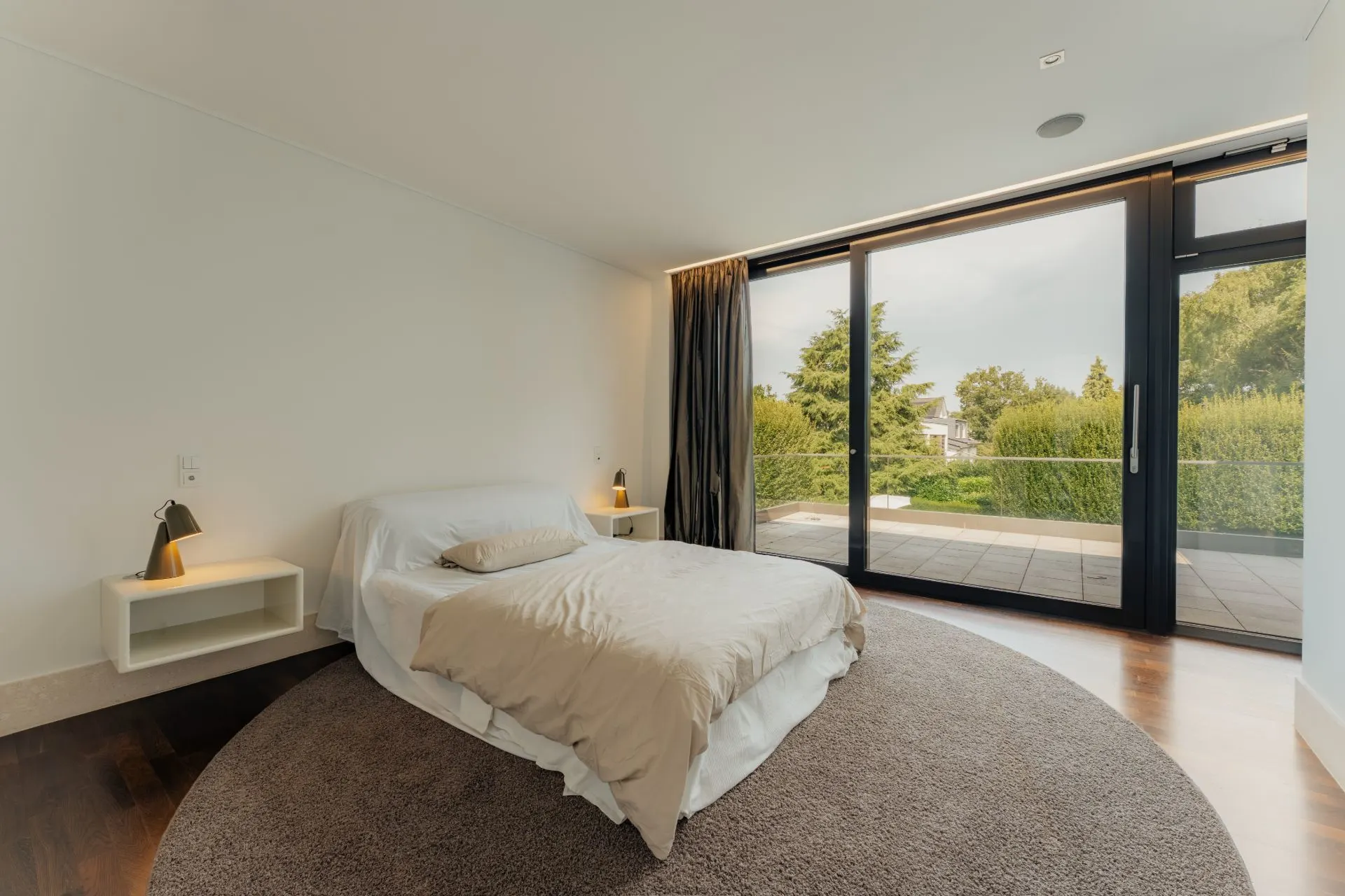 Schlafzimmer mit Doppelbett, Nachttischen und großen Fenstern mit Blick auf Terrasse und Garten.