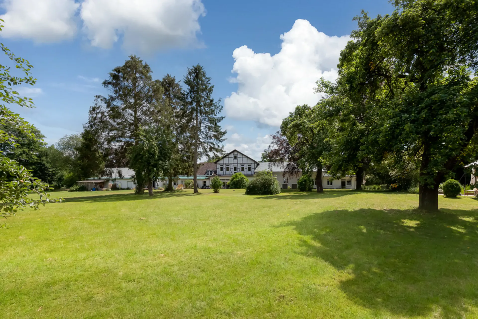 Großer Garten mit Bäumen und Wiese vor einem Wohnhaus an einem sonnigen Tag.