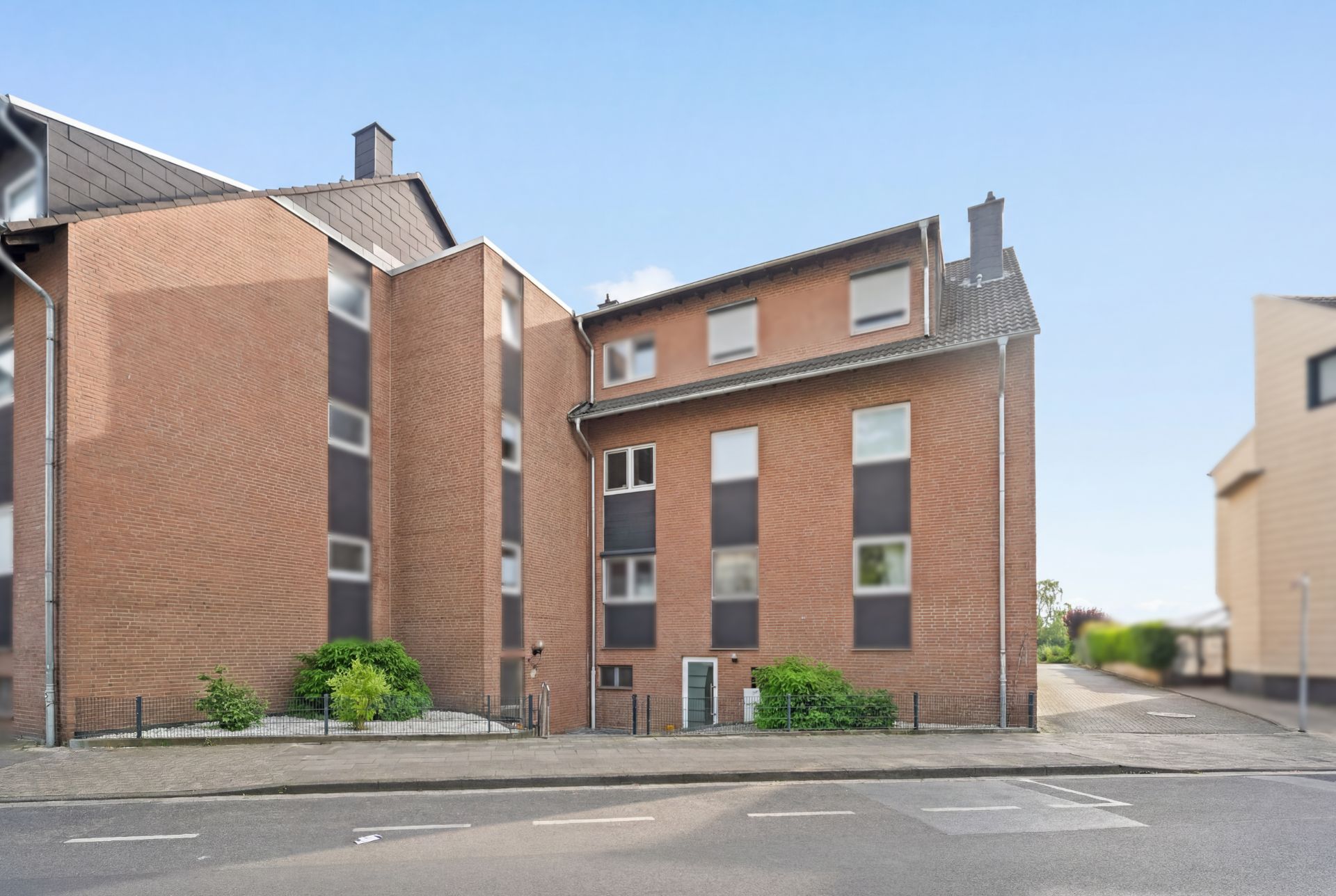 Mehrfamilienhaus aus rotem Backstein mit mehreren Fenstern und Eingängen an einer Straße.