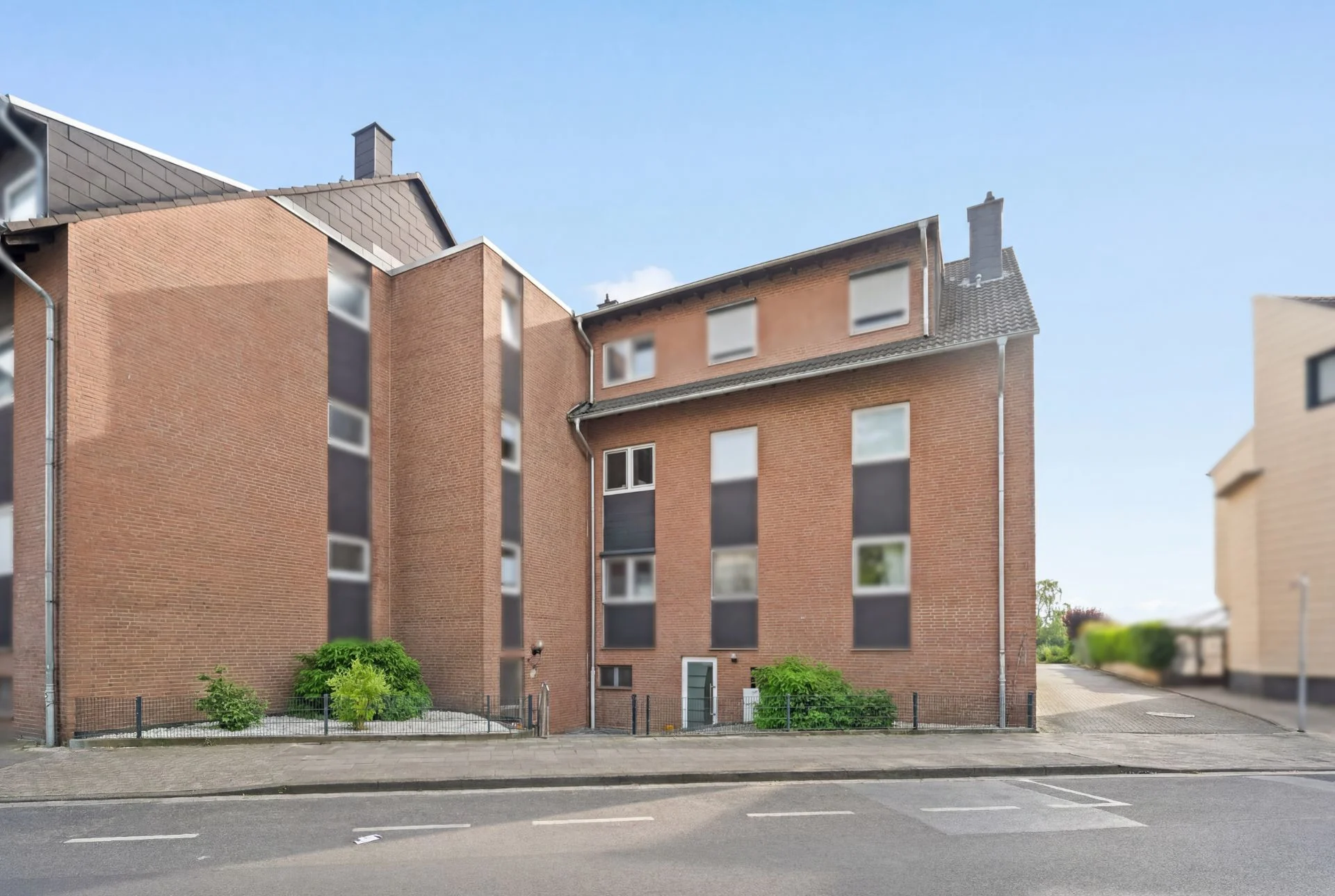Mehrfamilienhaus aus rotem Backstein mit mehreren Fenstern und Eingängen an einer Straße.