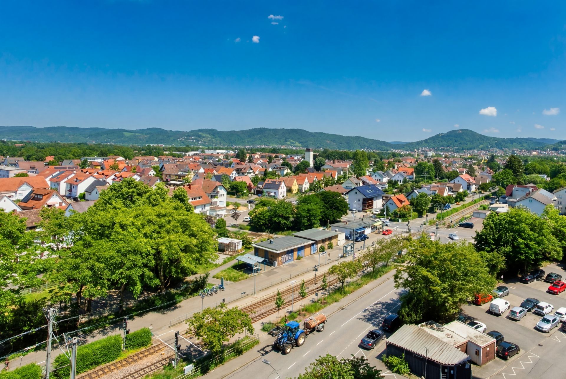 Luftaufnahme eines Wohngebiets mit roten Dächern, Straßen, Bäumen und Bahngleisen.