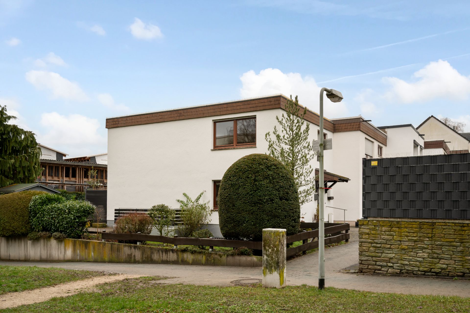 Weißes Wohnhaus mit Flachdach, Garten und Hecken an einer ruhigen Straße.
