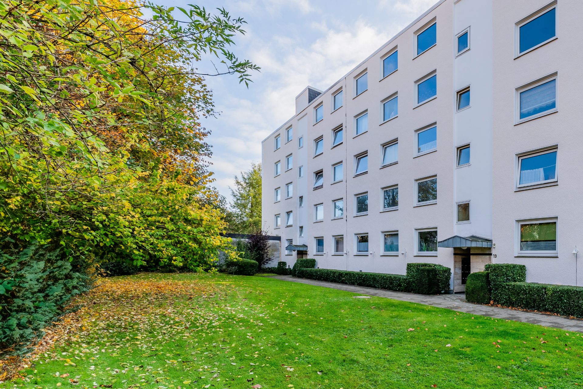 Mehrstöckiges Wohngebäude mit vielen Fenstern und grünem Garten davor.