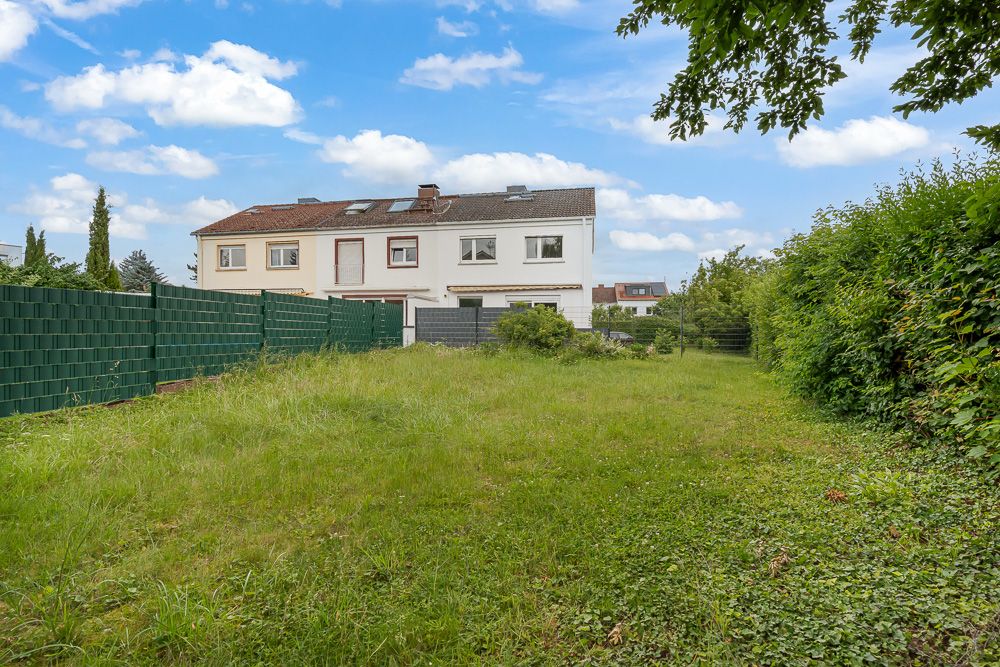 Grüner Garten mit Rasen hinter einem weißen Wohnhaus und Zaun an den Seiten.