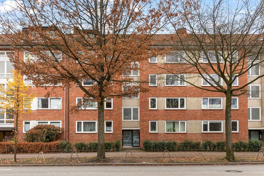 Vierstöckiges Wohnhaus mit roter Fassade, vielen Fenstern und Bäumen davor.