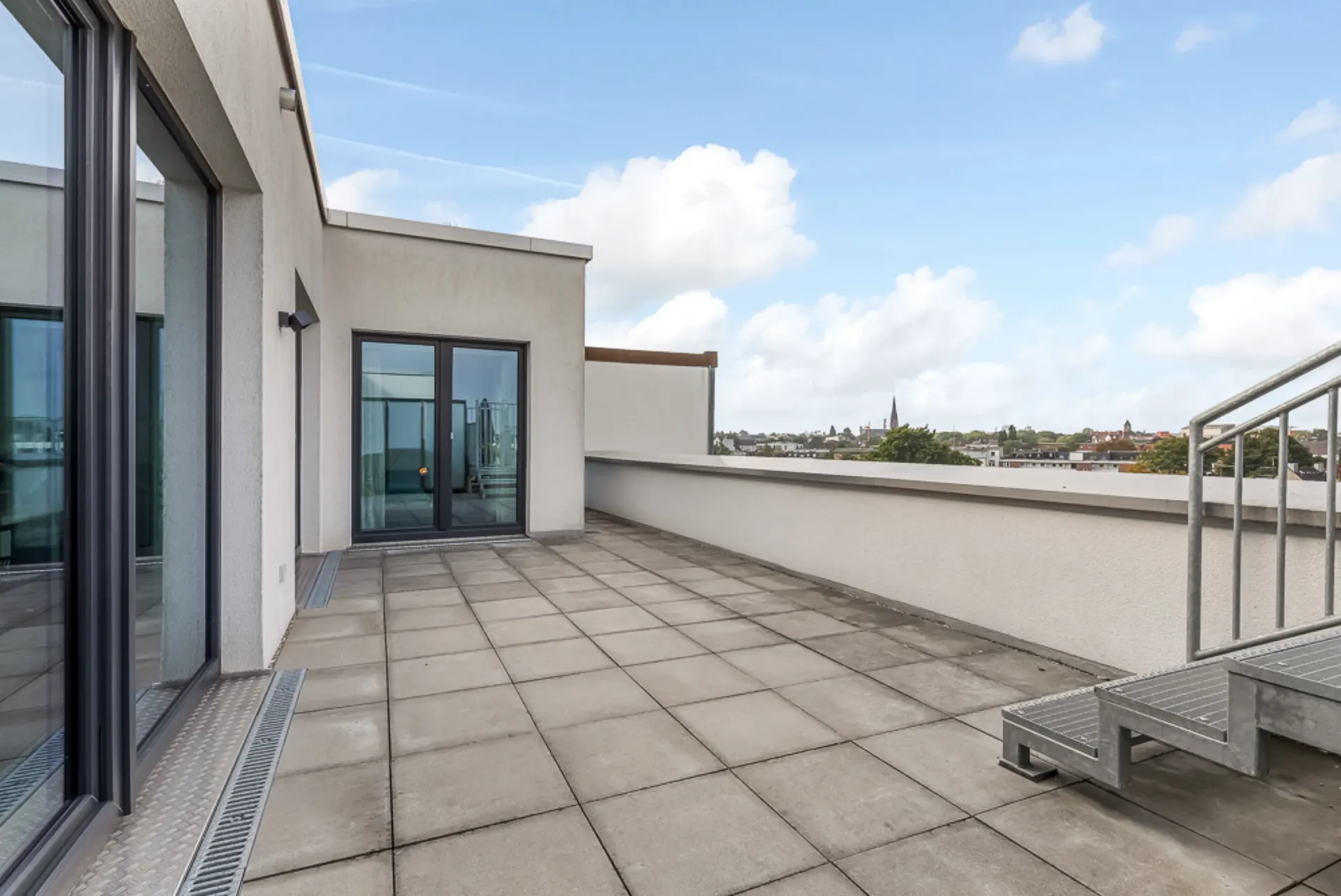 Große Dachterrasse mit Fliesenboden, Geländer und Blick über die Stadt.