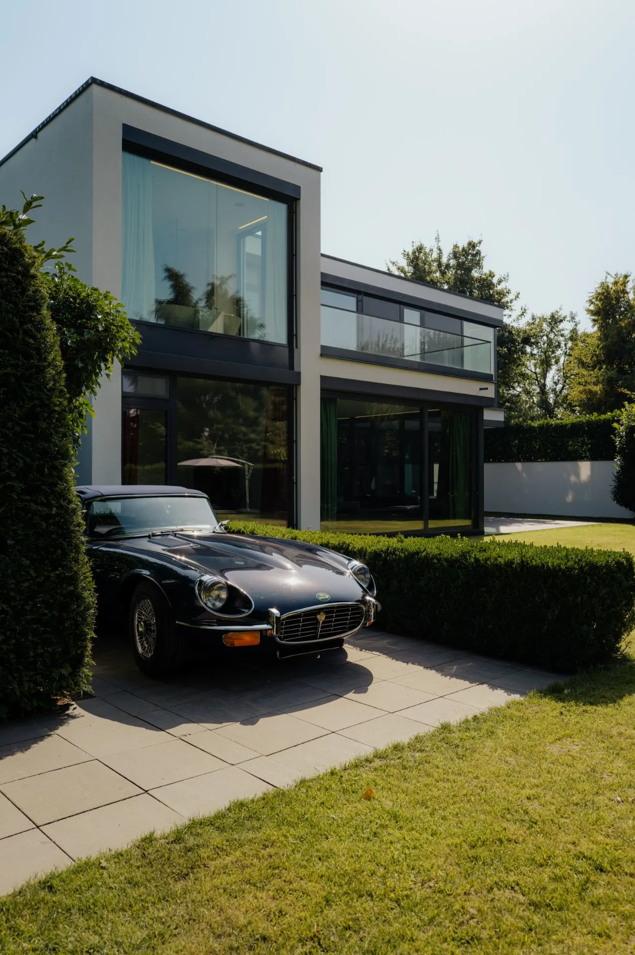 Modernes zweistöckiges Haus mit großen Fenstern und einem Oldtimer auf der Einfahrt.