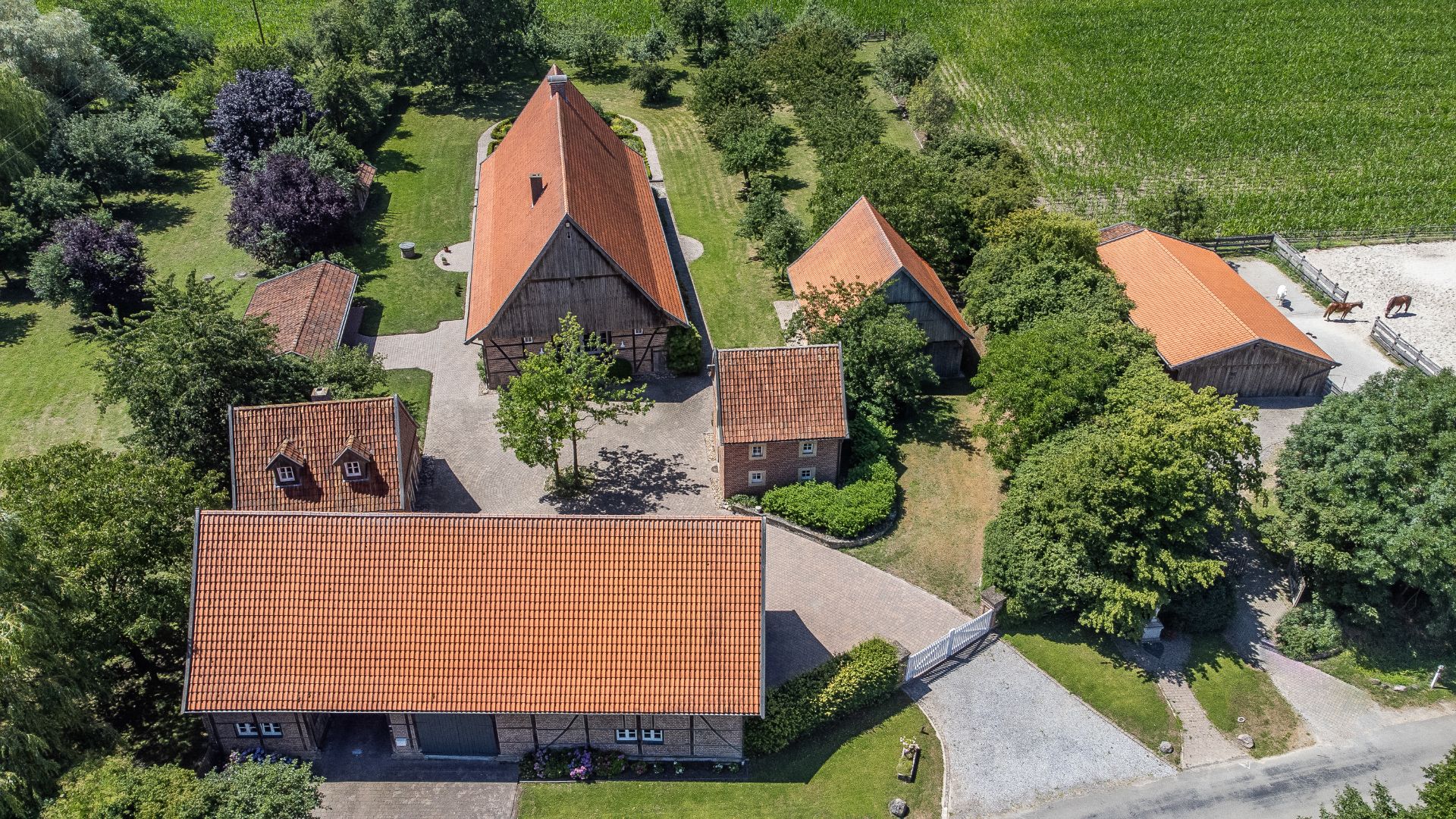 Luftaufnahme eines Anwesens mit mehreren Gebäuden und roten Dächern, umgeben von Bäumen und Feldern.