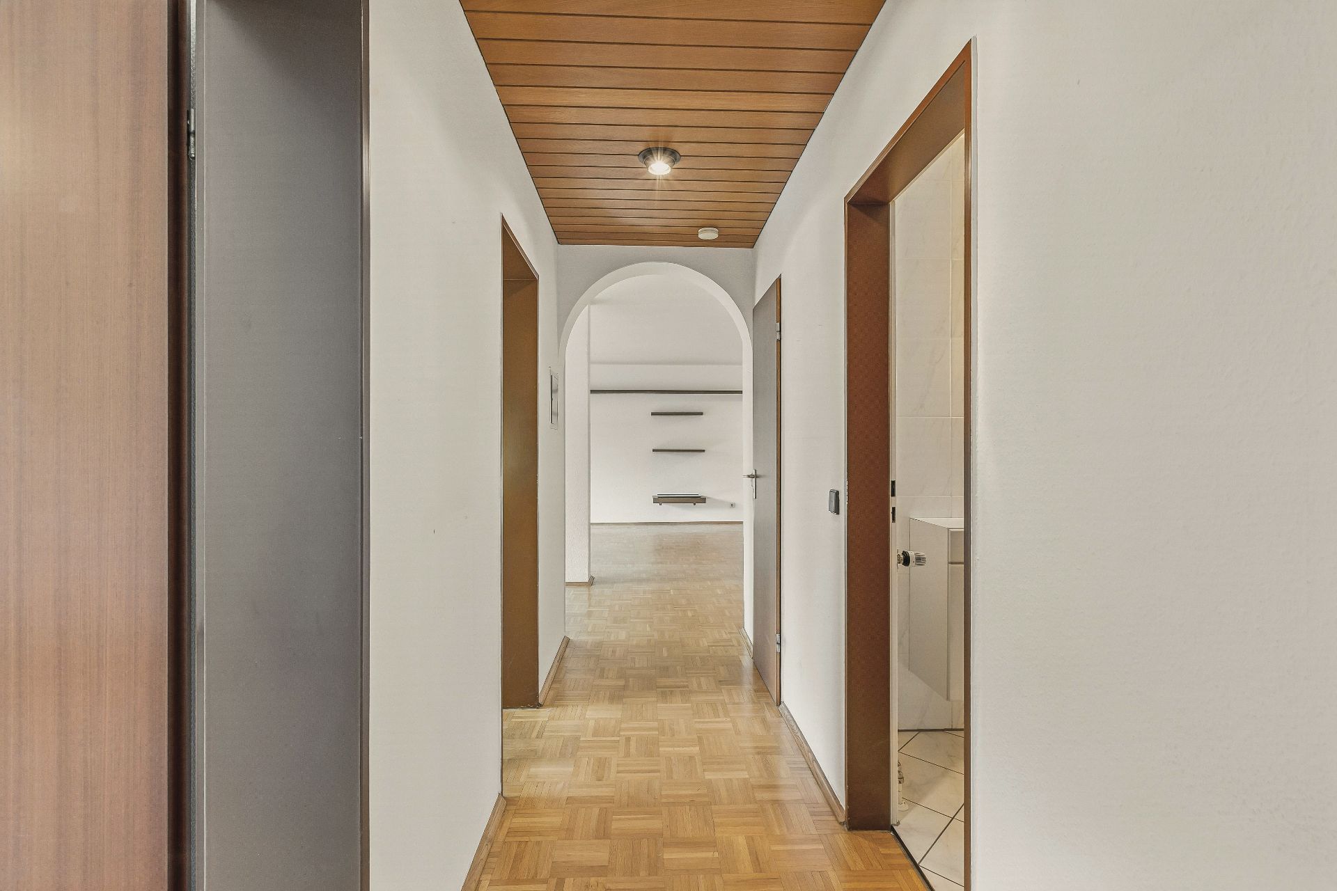 Heller Flur mit Holzdecke, Parkettboden und Türen zu weiteren Zimmern, Blick auf einen Raum mit Wandregalen.