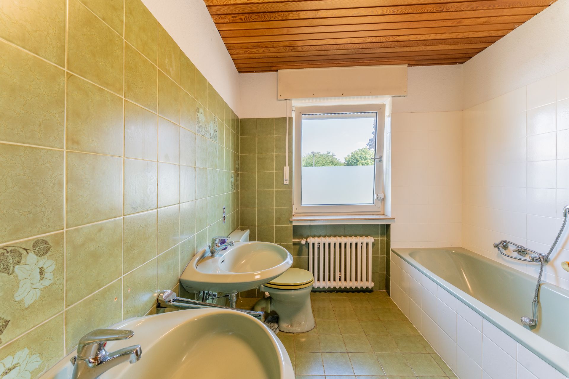 Badezimmer mit grünen Fliesen, zwei Waschbecken, Toilette, Badewanne und Fenster.