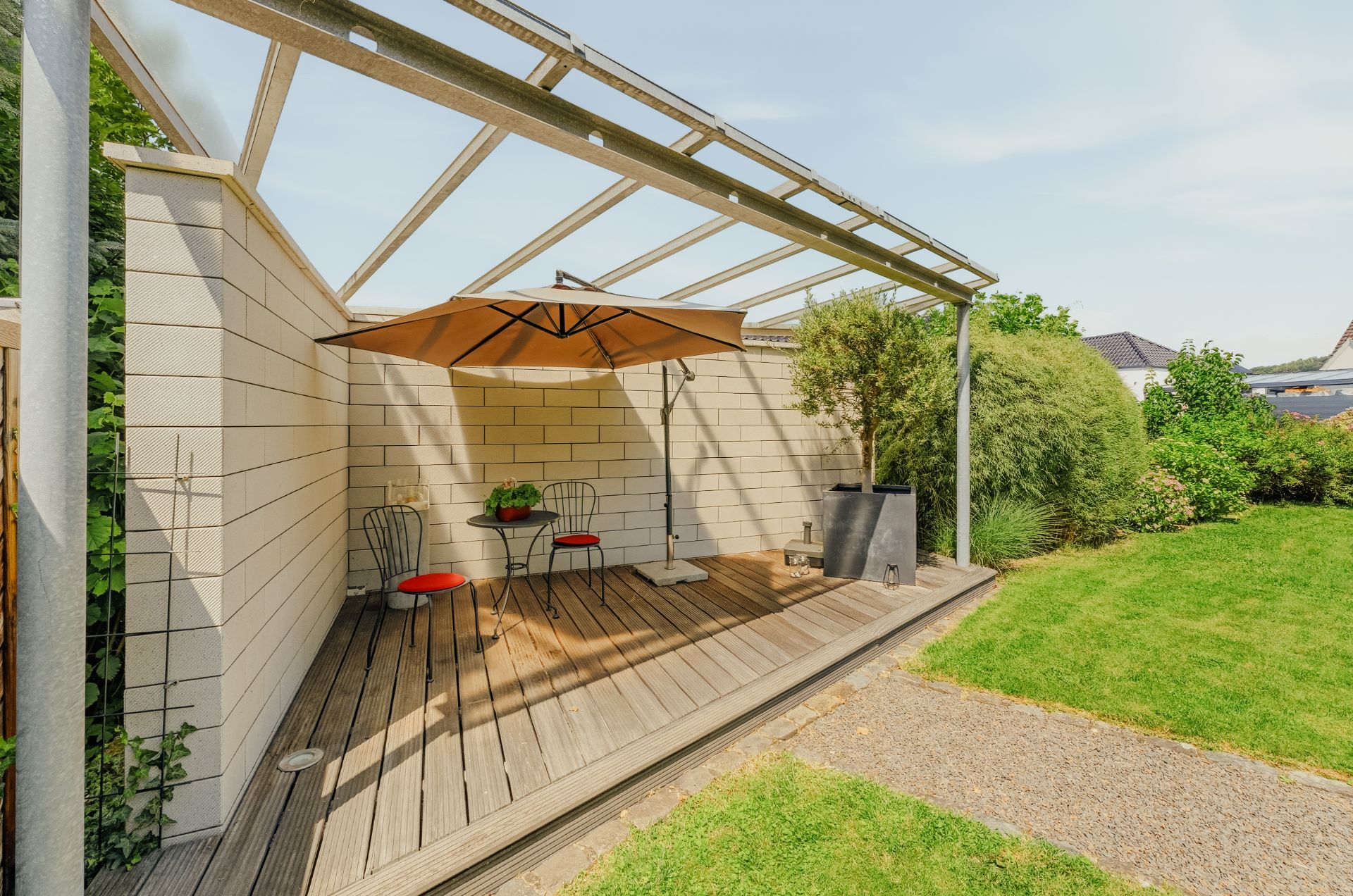 Überdachte Holzterrasse mit Tisch, zwei Stühlen und Sonnenschirm im Garten.