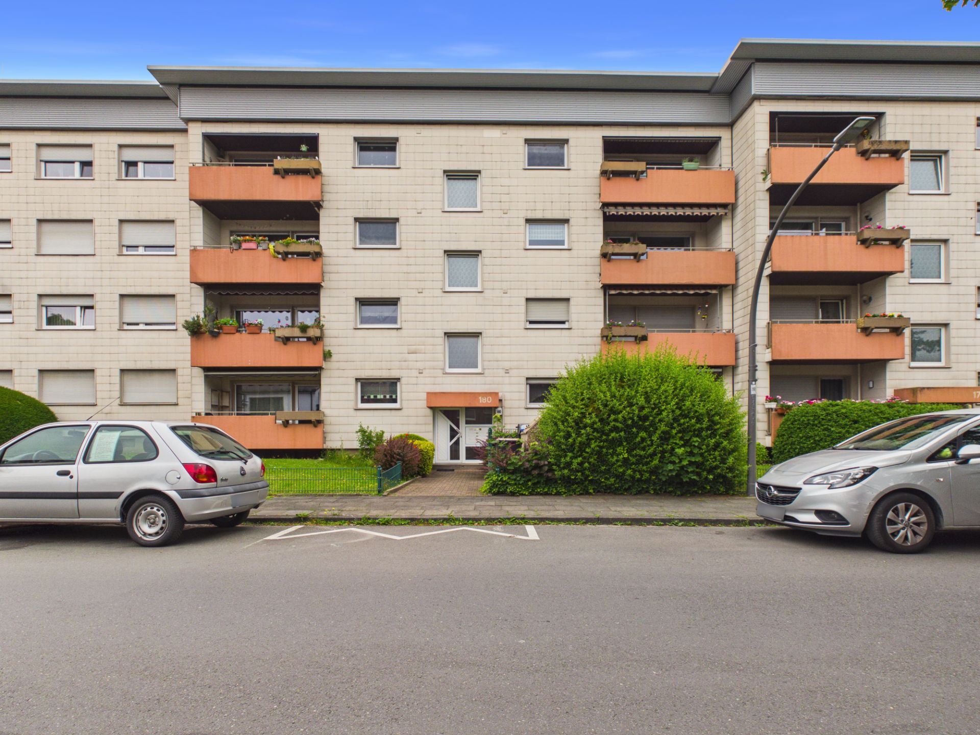 Mehrfamilienhaus mit mehreren Balkonen und geparkten Autos an der Straße.