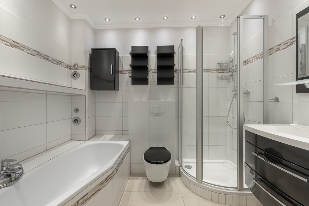 Modernes Badezimmer mit Badewanne, Dusche, Toilette und schwarzen Schränken.