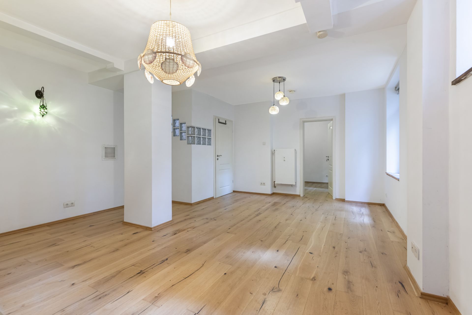 Heller Raum mit Holzboden, weißen Wänden und zwei modernen Deckenleuchten.