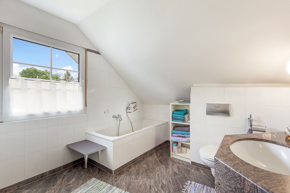 Modernes Badezimmer mit Badewanne, großem Fenster und Regal mit bunten Handtüchern.