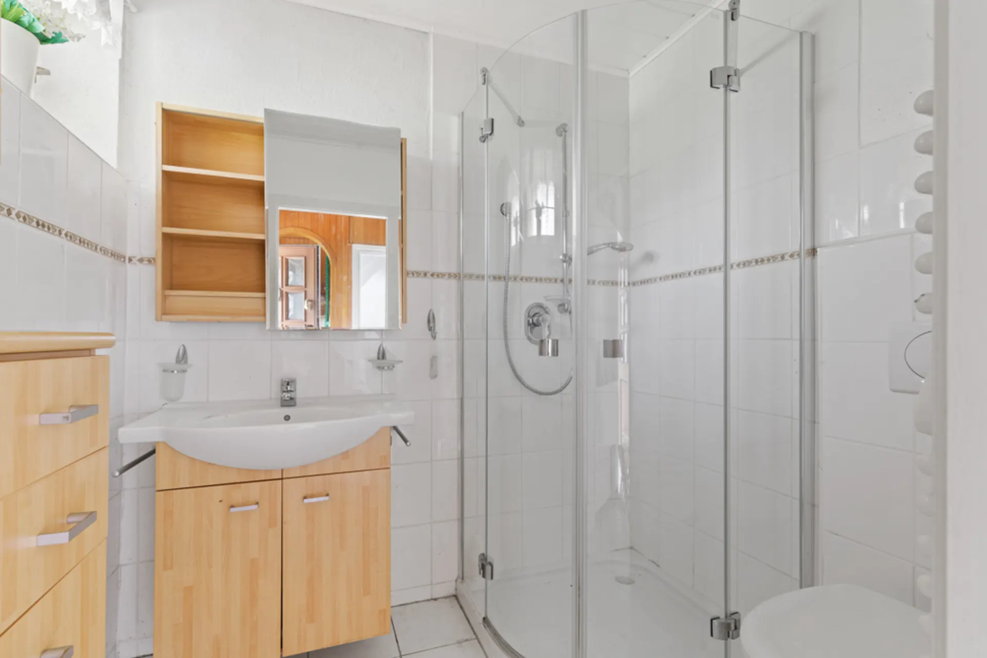 Helles Badezimmer mit Eckdusche, Waschbecken, Spiegelschrank und Holzunterschränken.