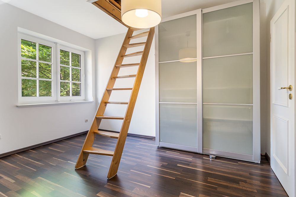 Helles Zimmer mit Holzleiter, großen Fenstern und Schrank mit Schiebetüren.