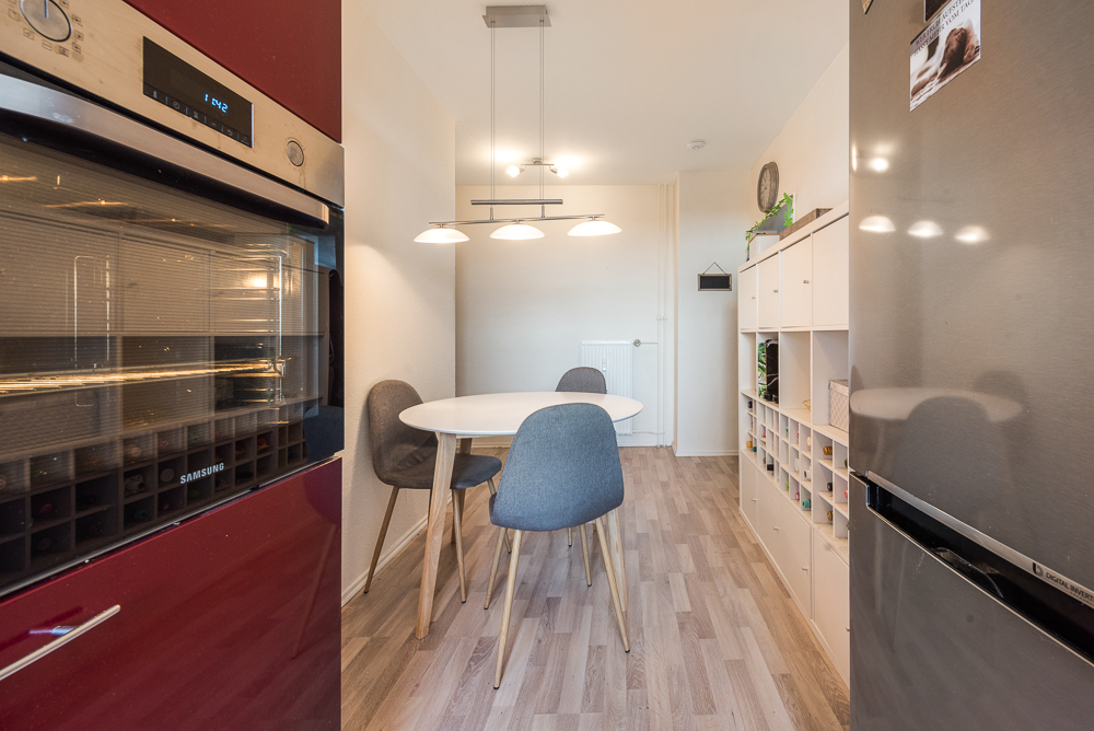 Moderne Küche mit Esstisch, vier Stühlen, offenem Regal, Backofen und Kühlschrank.