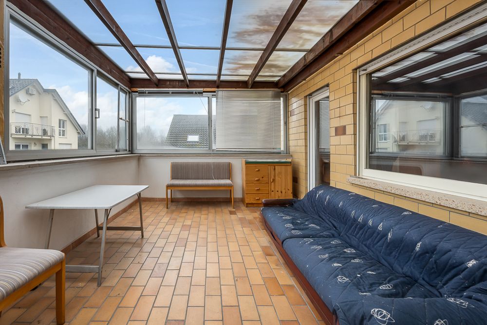 Veranda mit Ziegelboden, Sofa, Tisch, Stühlen und großen Fenstern.
