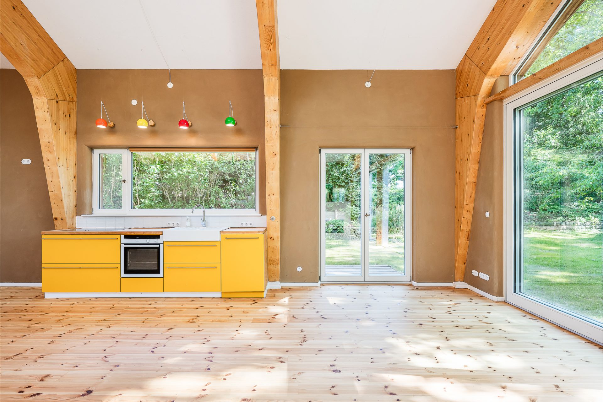 Helle Küche mit gelben Unterschränken, bunten Deckenlampen und großen Fenstern zum Garten.