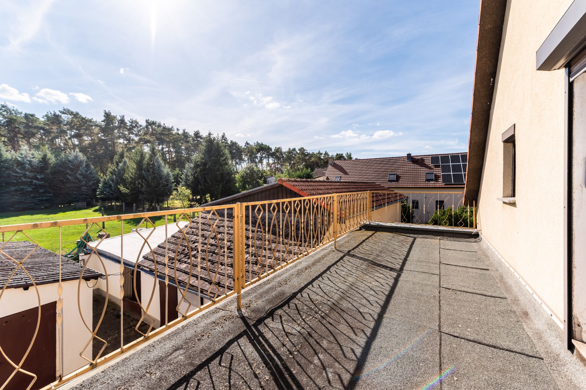 Balkon mit Geländer, Blick auf Nachbarhäuser und Bäume bei sonnigem Wetter.