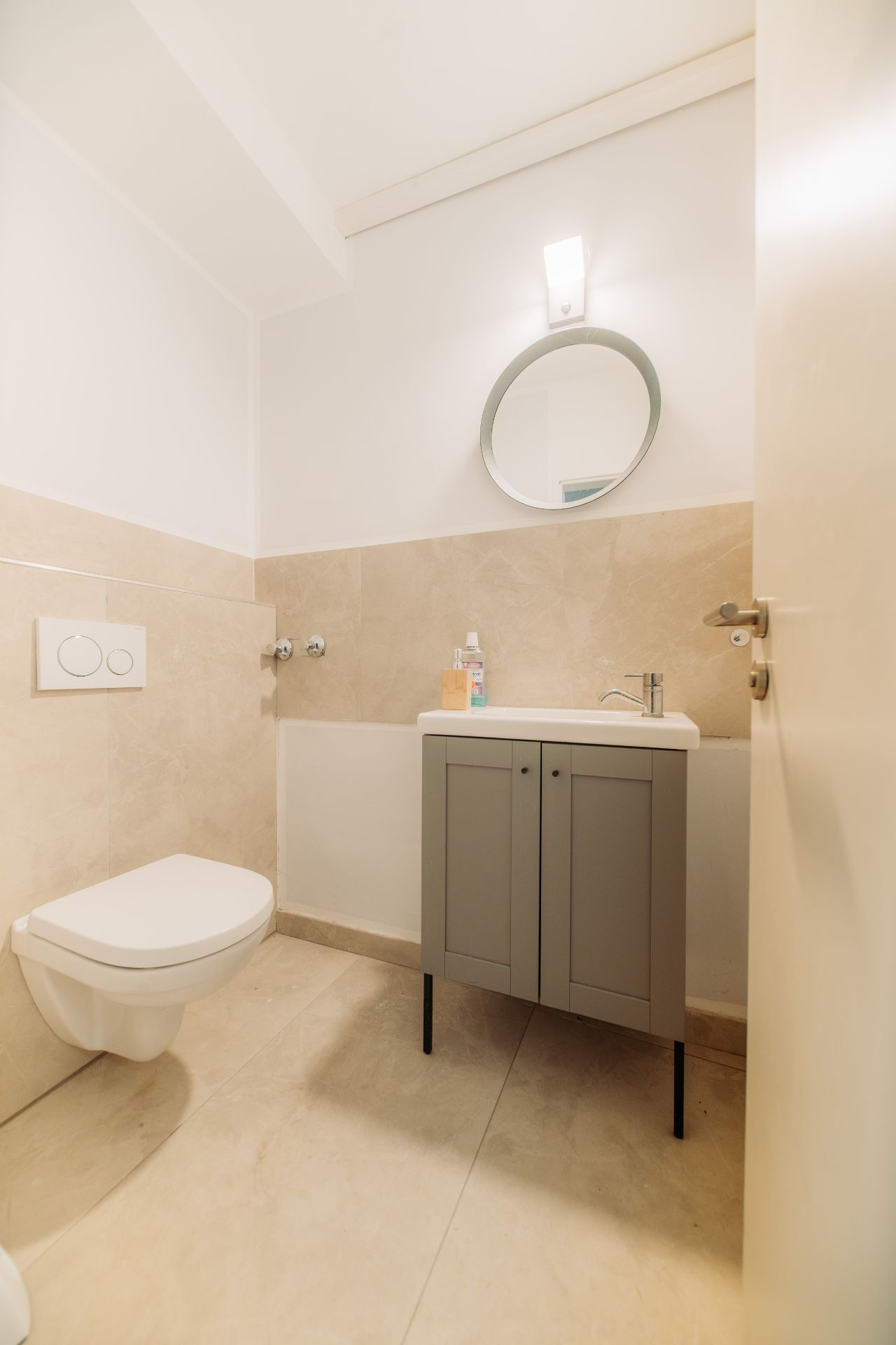 Modernes Badezimmer mit Hänge-WC, Waschbecken, Spiegel und grauem Unterschrank.