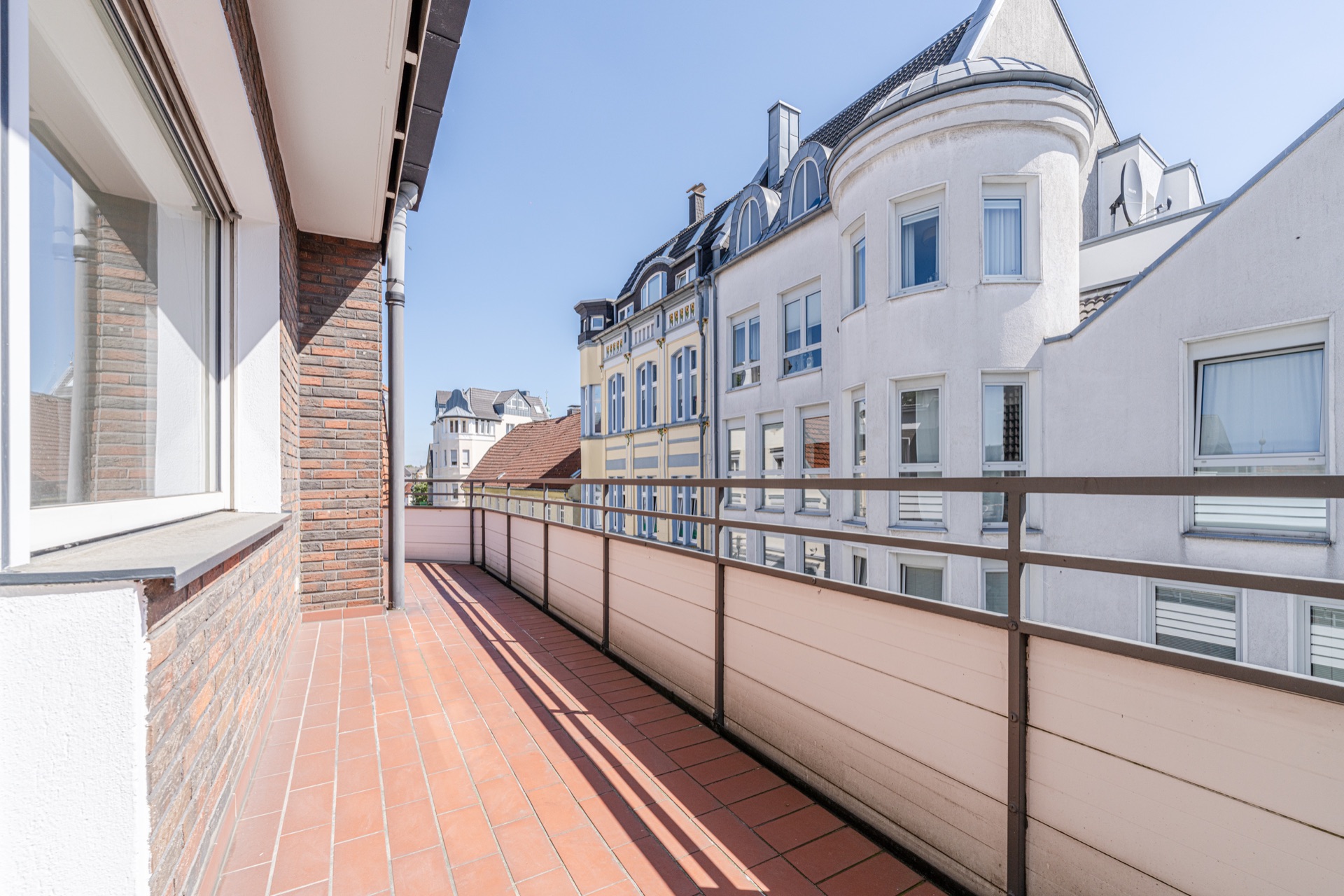 Großer Balkon mit roten Fliesen und Blick auf benachbarte Wohngebäude.